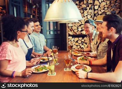 people, leisure, friendship and communication concept - group of happy smiling friends eating, drinking and talking at bar or pub