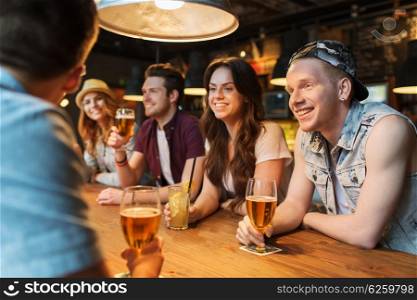 people, leisure, friendship and communication concept - group of happy smiling friends drinking beer and cocktails talking at bar or pub