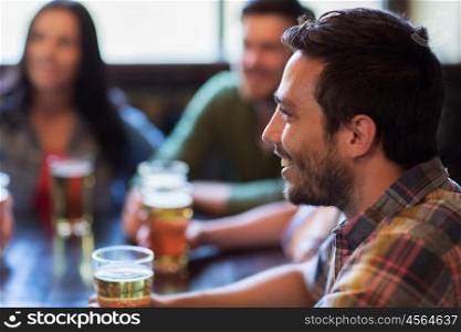people, leisure, friendship and communication concept - happy man with friends drinking beer at bar or pub