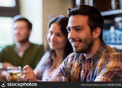 people, leisure, friendship and communication concept - happy man with friends drinking beer at bar or pub