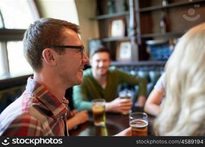 people, leisure, friendship and communication concept - happy young man drinking beer with friends at bar or pub