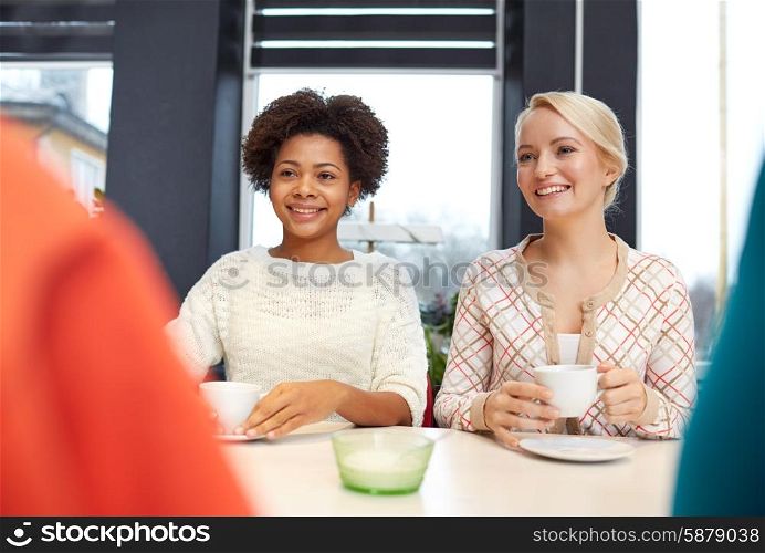 people, leisure, friendship and communication concept - happy young women meeting and drinking tea or coffee at cafe