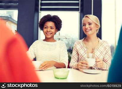 people, leisure, friendship and communication concept - happy young women meeting and drinking tea or coffee at cafe