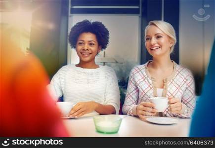 people, leisure, friendship and communication concept - happy young women meeting and drinking tea or coffee at cafe. happy young women drinking tea or coffee at cafe