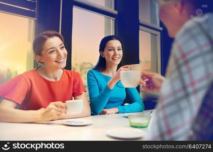 people, leisure, friendship and communication concept - happy young women meeting and drinking tea or coffee at cafe. happy young women drinking tea or coffee at cafe