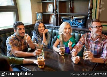 people, leisure, friendship and entertainment concept - happy friends drinking beer and watching sport game or football match at bar or pub