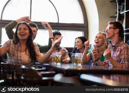 people, leisure, friendship and entertainment concept - happy friends with smartphones drinking beer and watching sport game or football match at bar or pub
