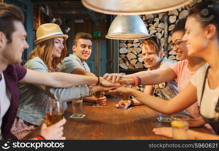 people, leisure, friendship and gesture concept - group of happy smiling friends with drinks putting hands on top of each other at bar or pub