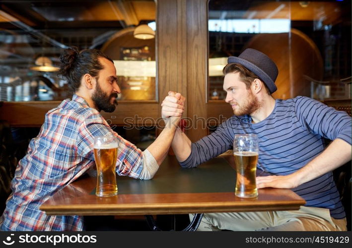 people, leisure, friendship and party concept - happy male friends drinking draft beer and arm wrestling at bar or pub and