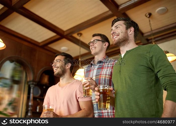 people, leisure, friendship and sport concept - happy male friends watching sport game or football match and drinking beer at bar or pub