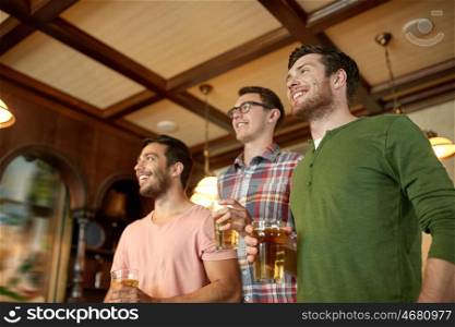 people, leisure, friendship and sport concept - happy male friends watching sport game or football match and drinking beer at bar or pub