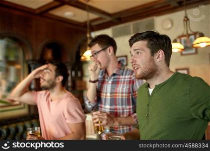 people, leisure, friendship and sport concept - upset male friends watching sport game or football match and drinking beer at bar or pub