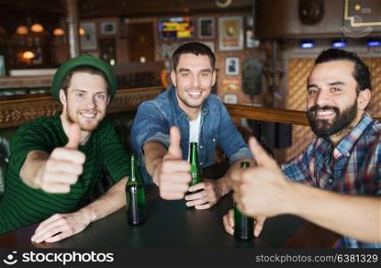 people, leisure, friendship and st patricks day concept - happy male friends drinking bottled beer and showing thumbs up at bar or pub. happy male friends drinking beer at bar or pub