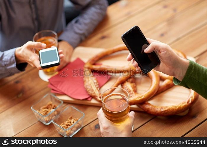 people, leisure, friendship and technology concept - close up of friends with smartphones and snacks drinking beer at bar or pub