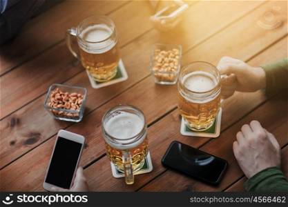 people, leisure, friendship and technology concept - close up of friends with smartphones and snacks drinking beer at bar or pub
