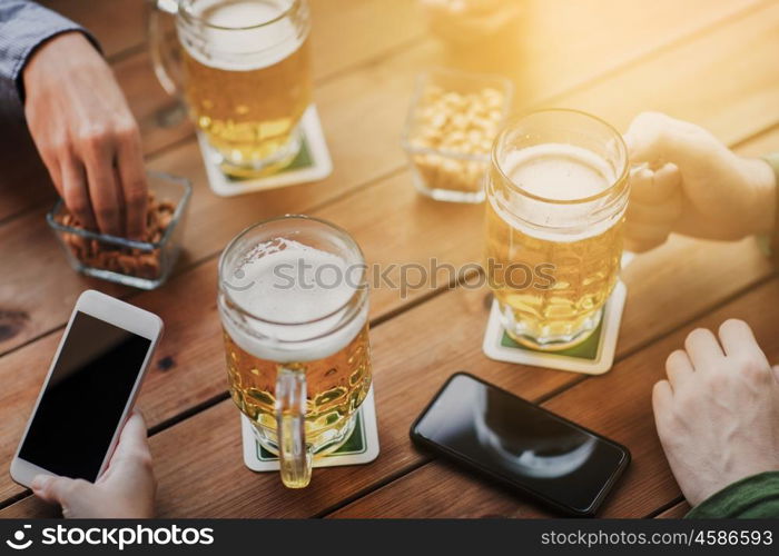 people, leisure, friendship and technology concept - close up of friends with smartphones and snacks drinking beer at bar or pub