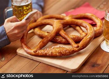 people, leisure, friendship and technology concept - close up of man with smartphone and pretzels on table drinking beer at bar or pub