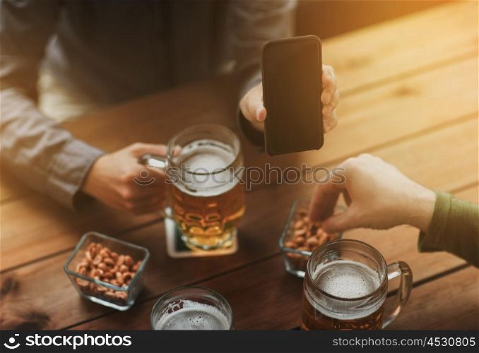 people, leisure, friendship and technology concept - close up of two male friends drinking beer with snacks and showing smartphone black blank screen at bar or pub