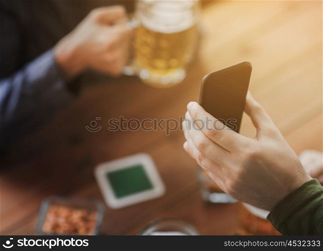 people, leisure, friendship and technology concept - close up of two male friends drinking beer with snacks and showing smartphone at bar or pub