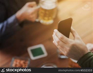 people, leisure, friendship and technology concept - close up of two male friends drinking beer with snacks and showing smartphone at bar or pub