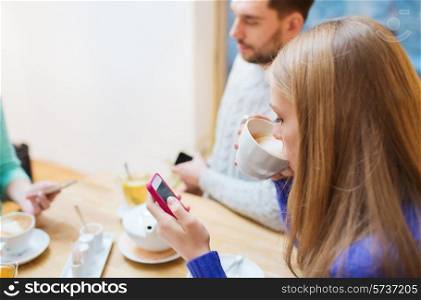 people, leisure, friendship and technology concept - couple with smartphones meeting and drinking tea at cafe