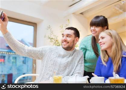 people, leisure, friendship and technology concept - group of happy friends with smartphone taking selfie and drinking tea at cafe
