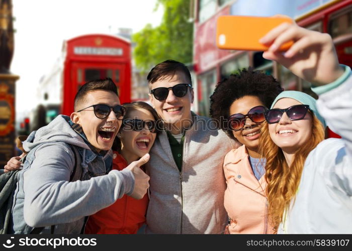 people, leisure, friendship and technology concept - group of smiling teenage friends taking selfie with smartphone over london city street background
