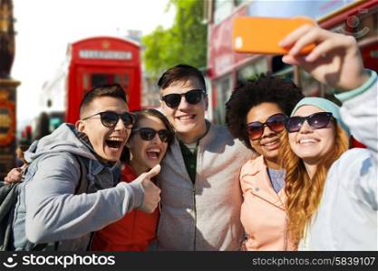 people, leisure, friendship and technology concept - group of smiling teenage friends taking selfie with smartphone over london city street background