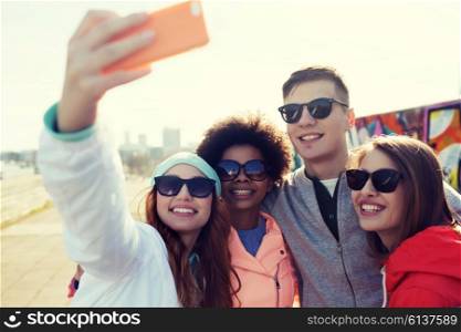 people, leisure, friendship and technology concept - group of smiling teenage friends taking selfie with smartphone outdoors