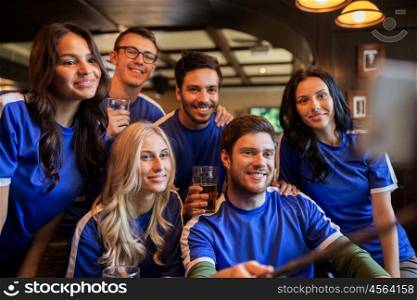 people, leisure, friendship and technology concept - happy friends or football fans taking picture by smartphone selfie stick and drinking beer at sport at bar or pub