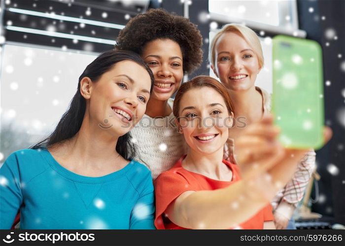 people, leisure, friendship and technology concept - happy young women taking selfie with smartphone over snow effect