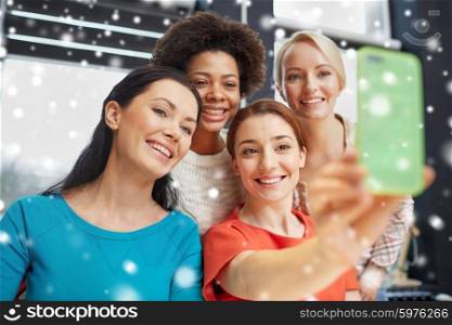 people, leisure, friendship and technology concept - happy young women taking selfie with smartphone over snow effect