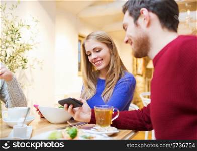 people, leisure, friendship and technology concept - smiling couple with smartphones meeting and drinking tea at cafe
