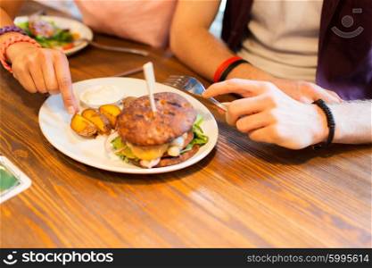 people, leisure, friendship, eating and food concept - close up of friends hands with burger at bar or pub