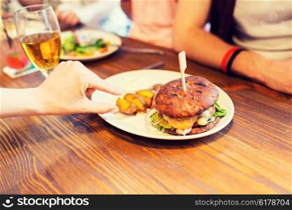 people, leisure, friendship, eating and food concept - close up of friends hands with burger at bar or pub