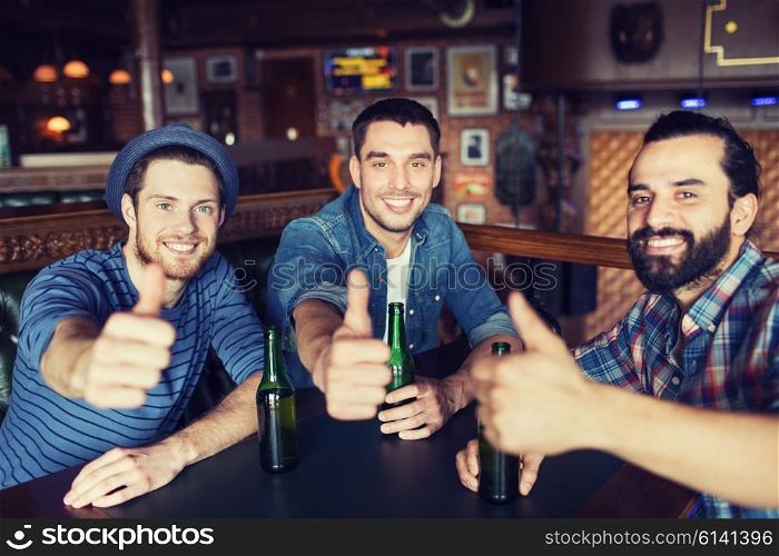 people, leisure, friendship, gesture and bachelor party concept - happy male friends drinking bottled beer and showing thumbs up at bar or pub