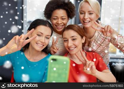 people, leisure, friendship, gesture and technology concept - happy young women taking selfie with smartphone and showing victory gesture over snow effect