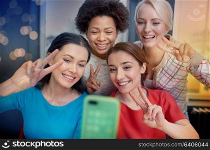 people, leisure, friendship, gesture and technology concept - happy young women taking selfie with smartphone and showing victory gesture. happy young women taking selfie with smartphone