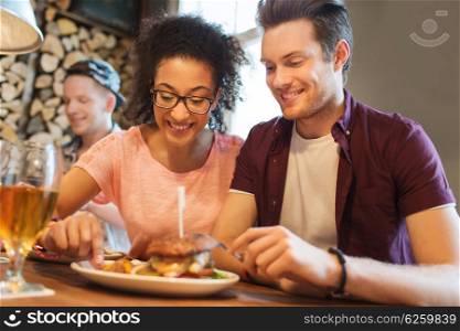 people, leisure, friendship, party and communication concept - group of happy smiling friends eating burger together at bar or pub