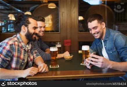 people, leisure, friendship, technology and bachelor party concept - happy male friends with smartphone drinking beer at bar or pub