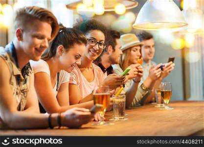 people, leisure, friendship, technology and communication concept - group of happy smiling friends with smartphones and drinks at bar or pub