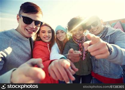 people, leisure, gesture and teenage concept - group of happy teenage friends pointing fingers on city street