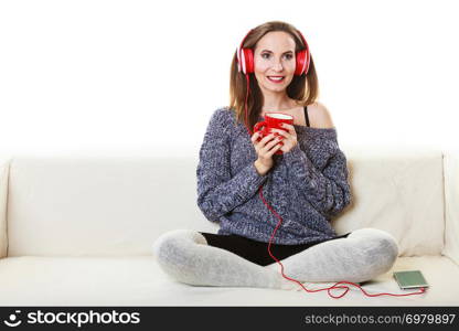 People leisure relax concept. Woman casual style red big headphones listening music mp3, sitting on couch at home relaxing drinking hot tea coffee