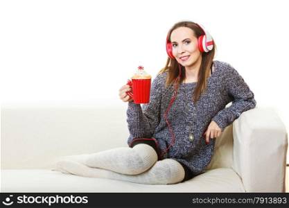 People leisure relax concept. Woman casual style red big headphones listening music mp3, sitting on couch at home relaxing drinking hot tea coffee