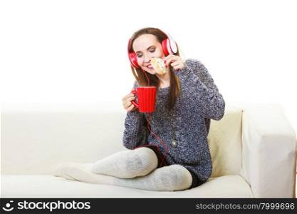 People leisure relax concept. Woman casual style red big headphones listening music mp3, sitting on couch at home relaxing drinking hot tea coffee