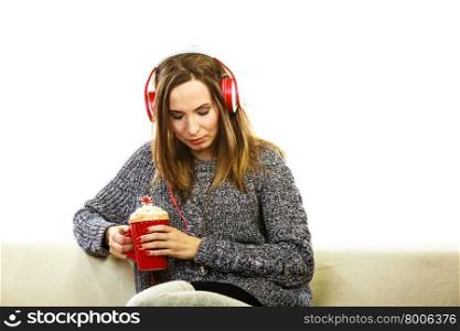 People leisure relax concept. Woman casual style red big headphones listening music mp3, sitting on couch with mug in deep thought
