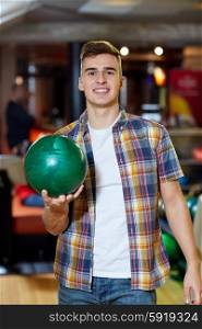 people, leisure, sport and entertainment concept - happy young man holding ball in bowling club