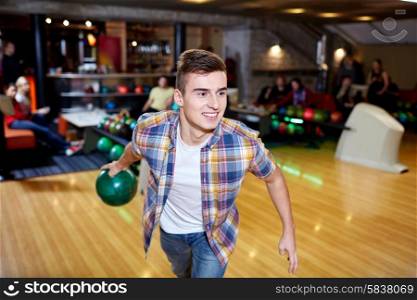 people, leisure, sport and entertainment concept - happy young man throwing ball in bowling club