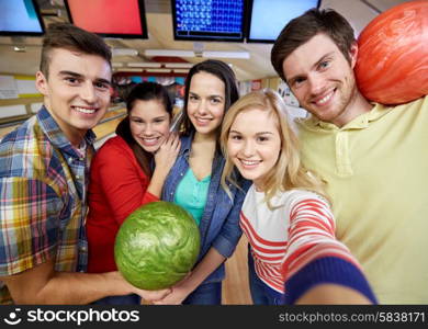 people, leisure, sport, friendship and entertainment concept - happy friends taking selfie with camera or smartphone in bowling club