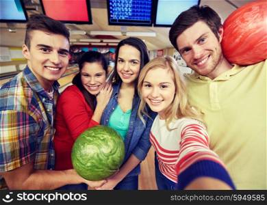 people, leisure, sport, friendship and entertainment concept - happy friends taking selfie with camera or smartphone in bowling club